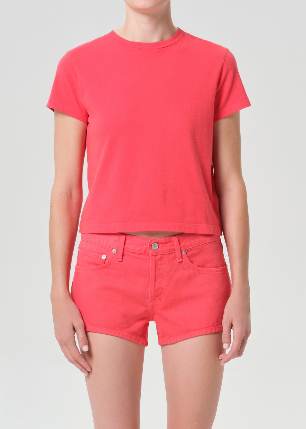 Person wearing a bright pink t-shirt and shorts on a light gray background