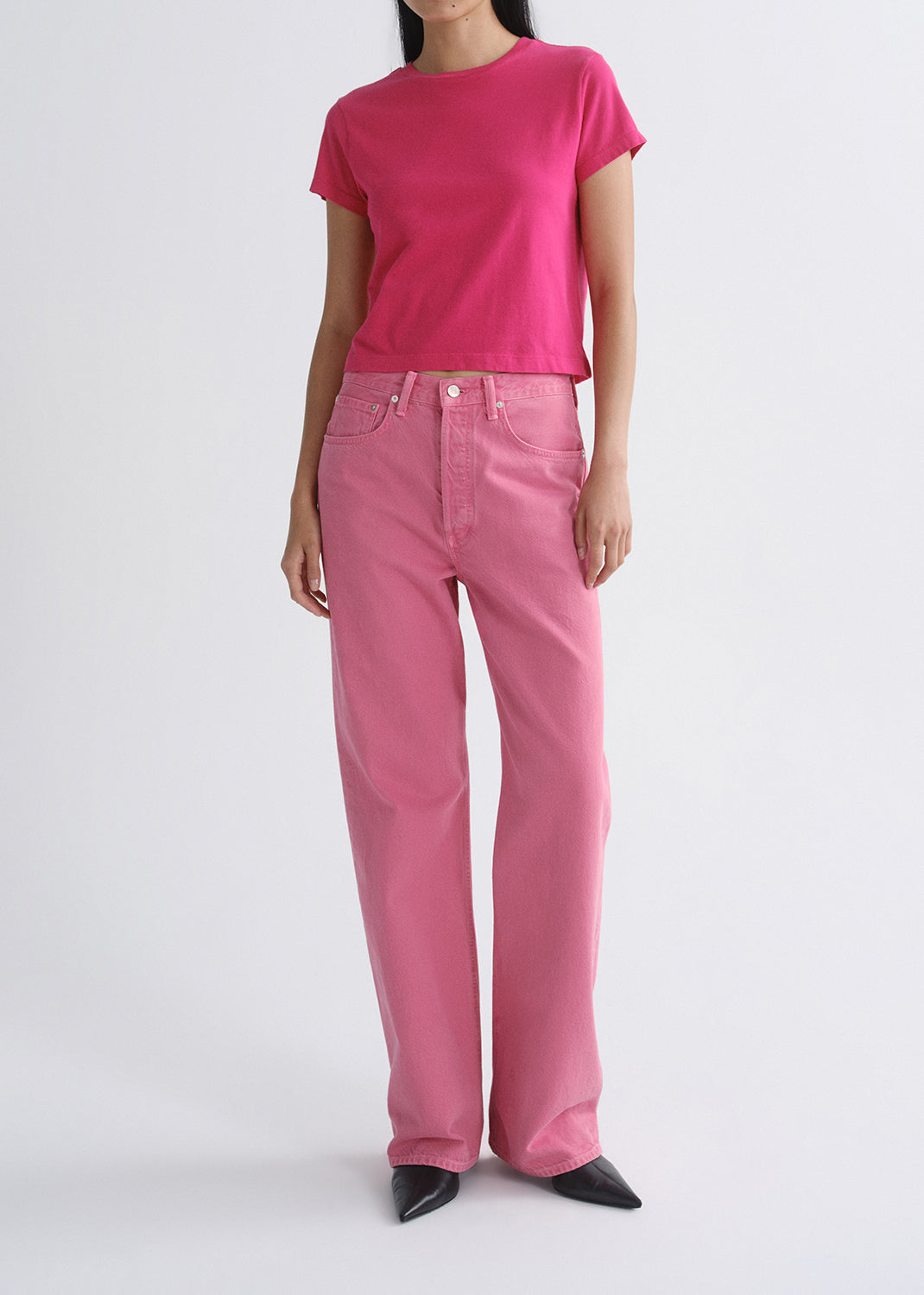 Person wearing a bright pink short sleeve crewneck tee with light pink straight leg jeans on a grey background