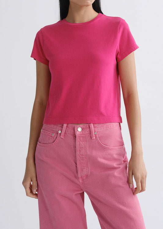 Person wearing a bright pink short sleeve crewneck tee on a grey background