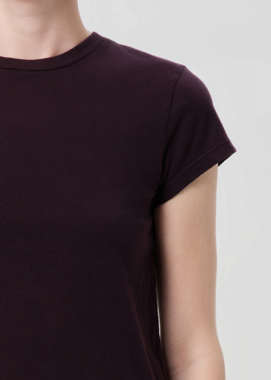 Close-up of a person wearing a dark purple t-shirt against a light gray background