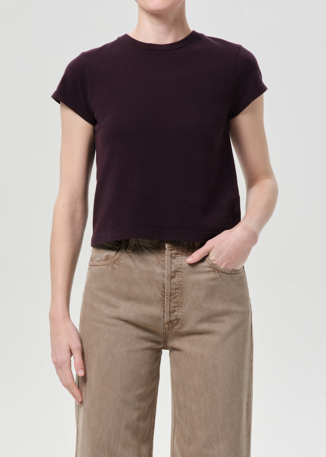 Person wearing a dark purple t-shirt and beige pants on a light gray background