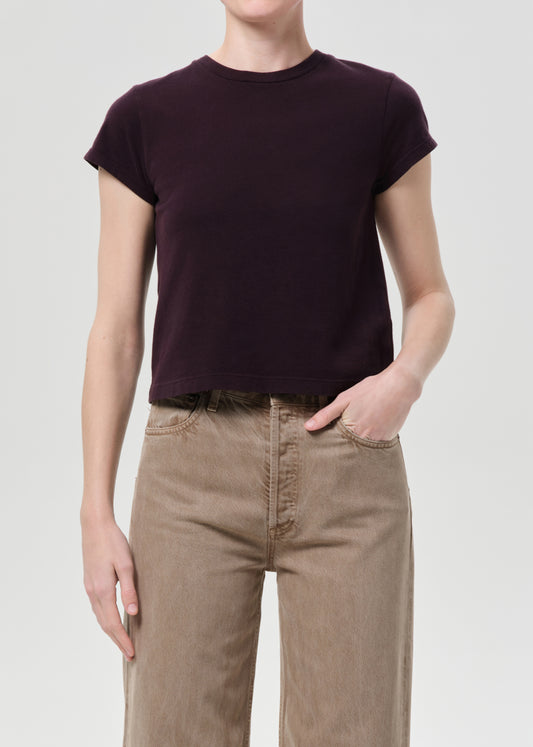 Person wearing a dark purple t-shirt and beige pants on a light gray background