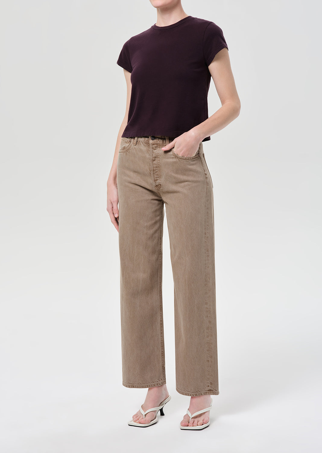Person wearing a dark purple t-shirt and beige pants on a white background