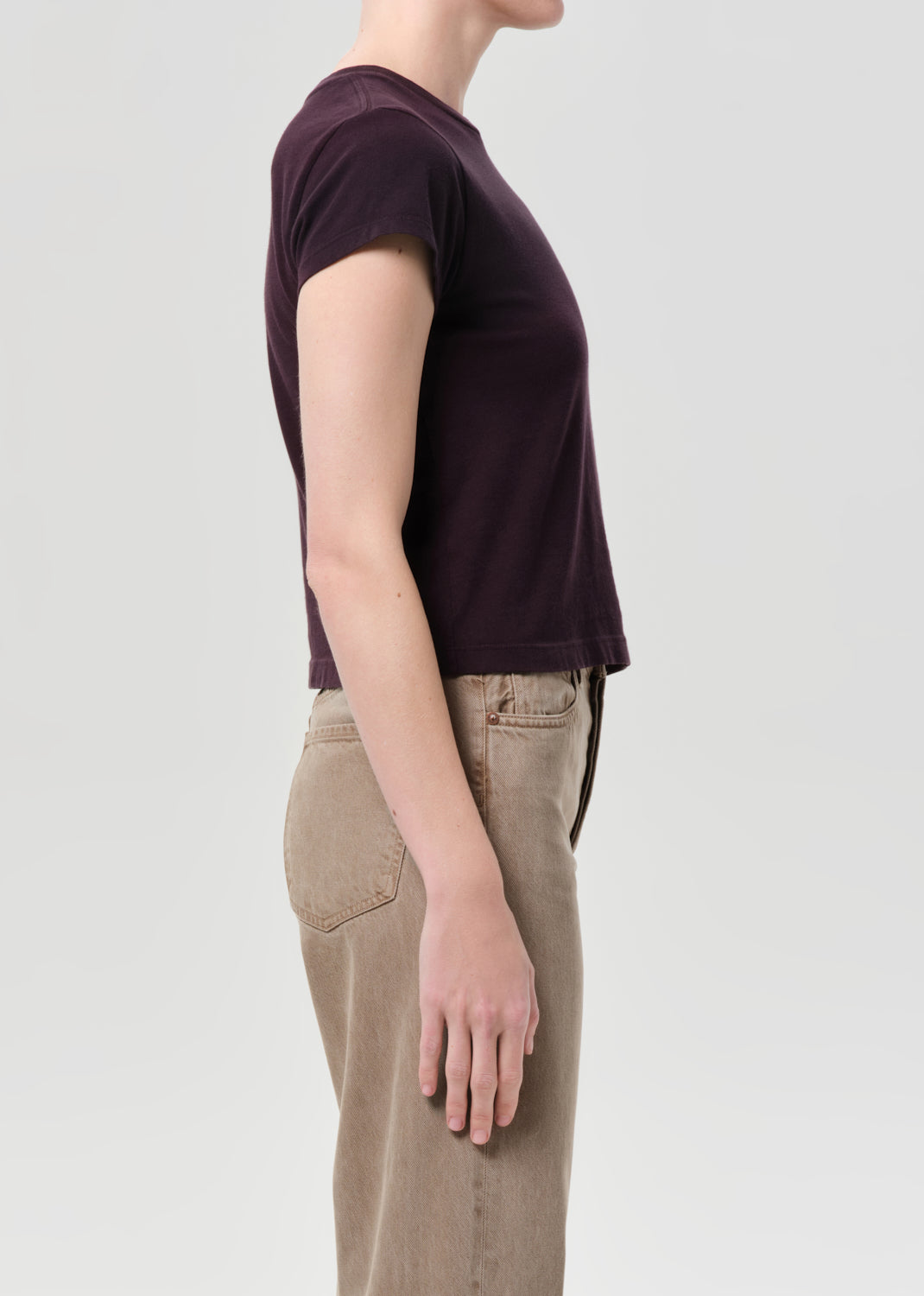 Person wearing a dark purple t-shirt and beige pants on a light gray background