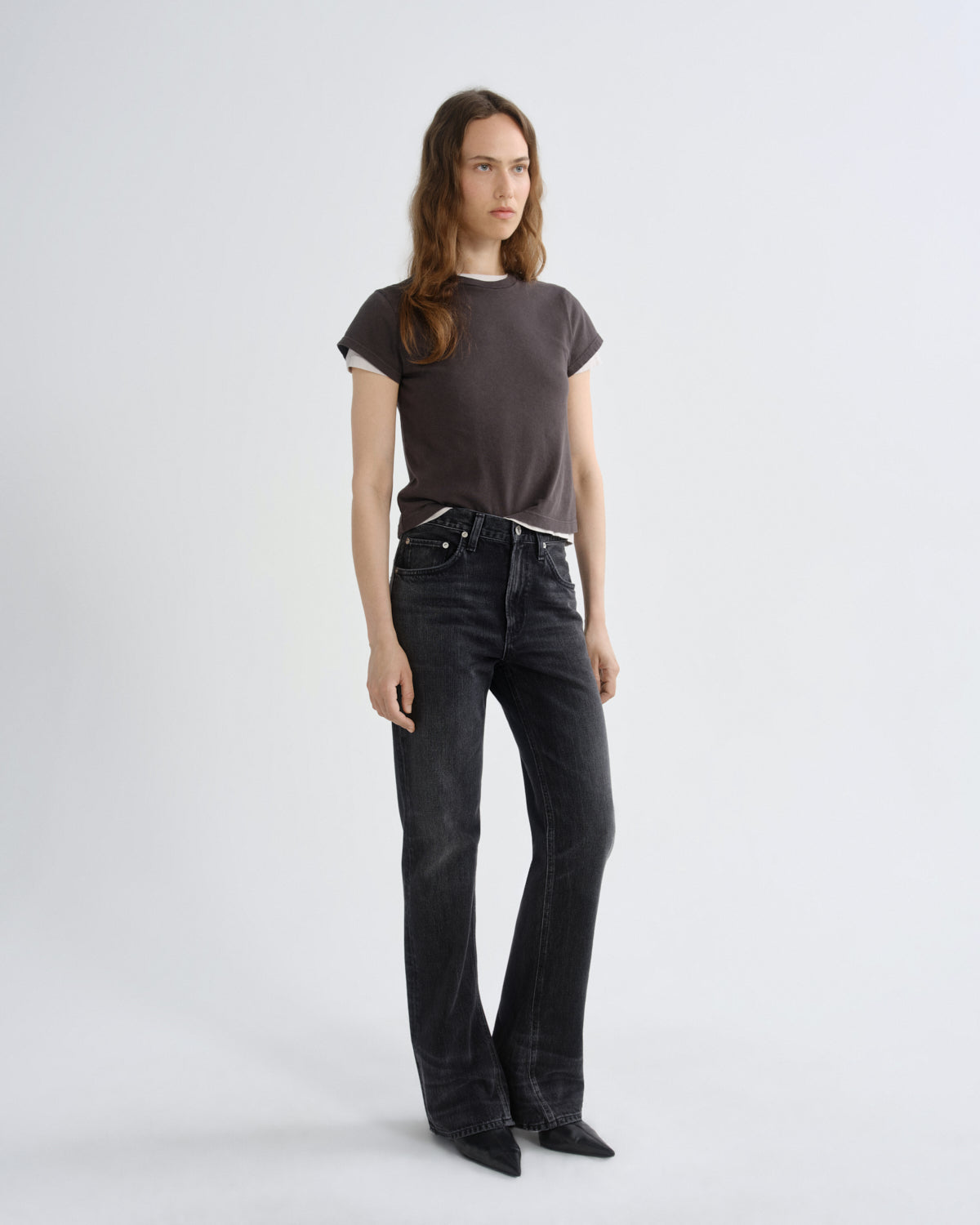 A woman modeling a dark brown short-sleeve t-shirt with white ribbed trim and black wide-leg jeans against a light gray studio background.