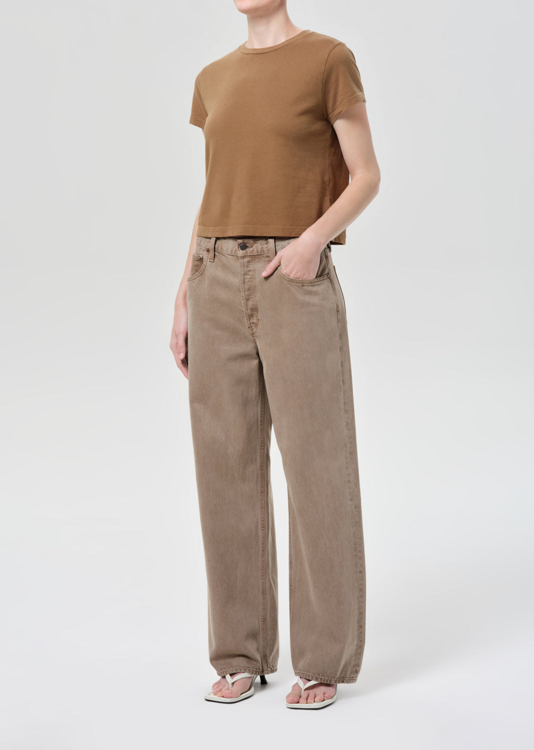 Person wearing a brown t-shirt and beige pants on a white background