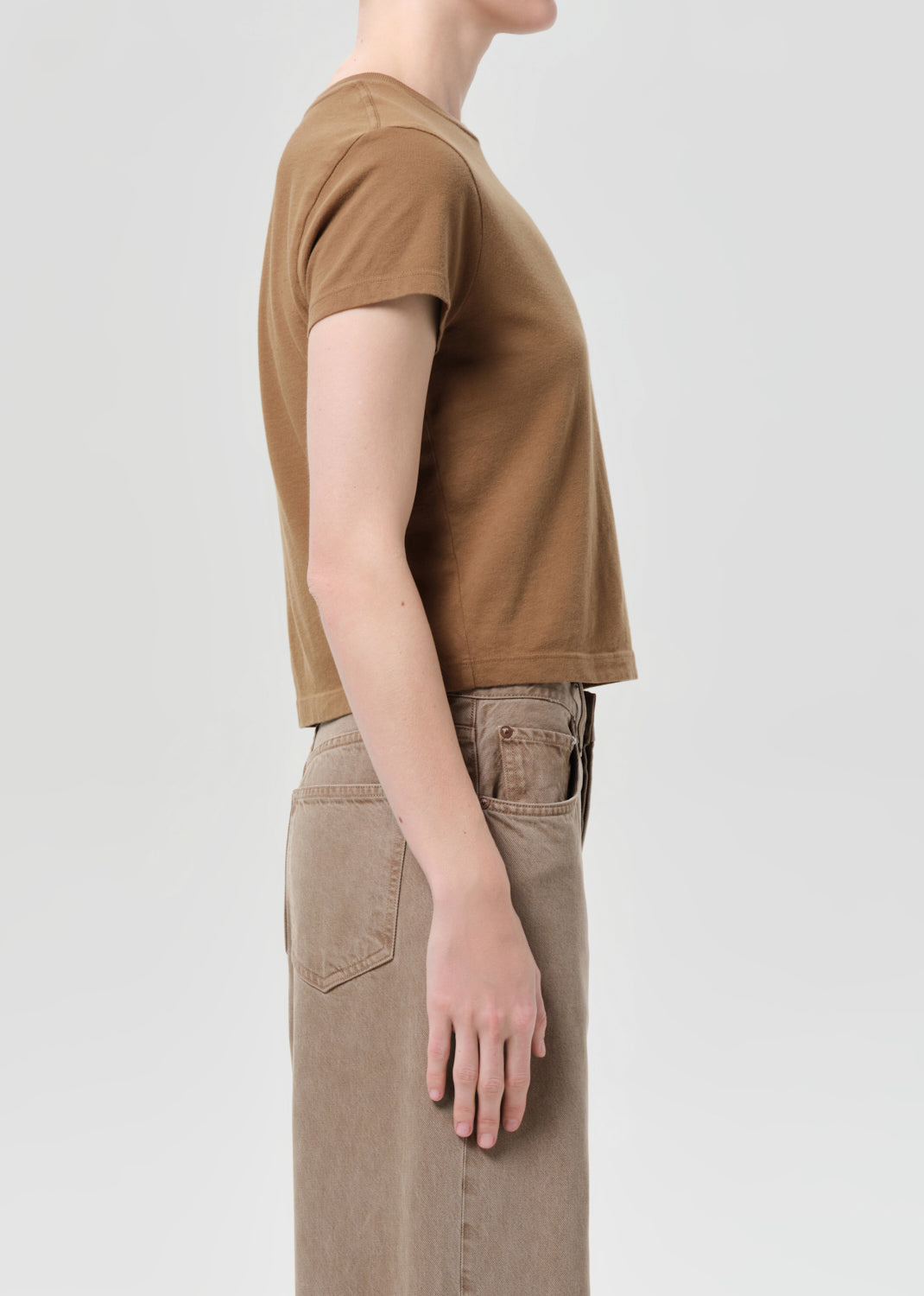 Person wearing a brown t-shirt and beige pants on a light gray background
