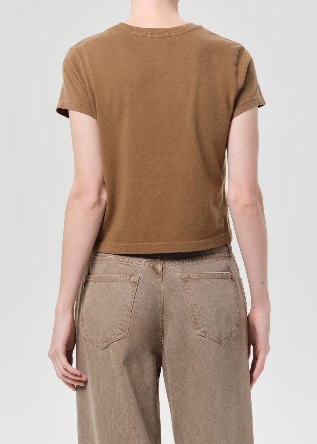 Person wearing a brown t-shirt and beige pants on a white background