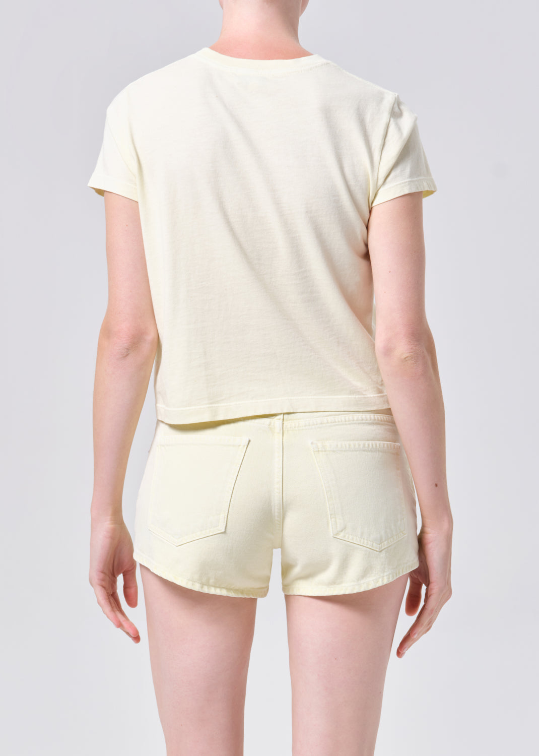 Person wearing a light yellow t-shirt and shorts set on a plain background