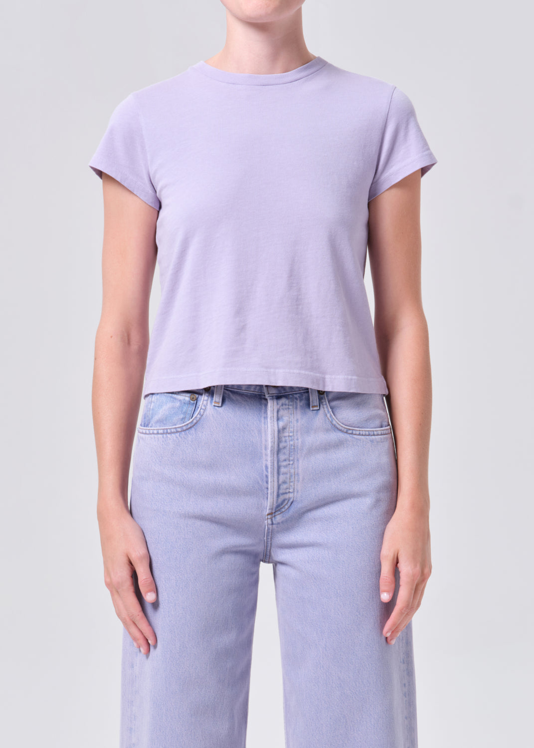 Person wearing a light purple t-shirt and light blue jeans on a plain background