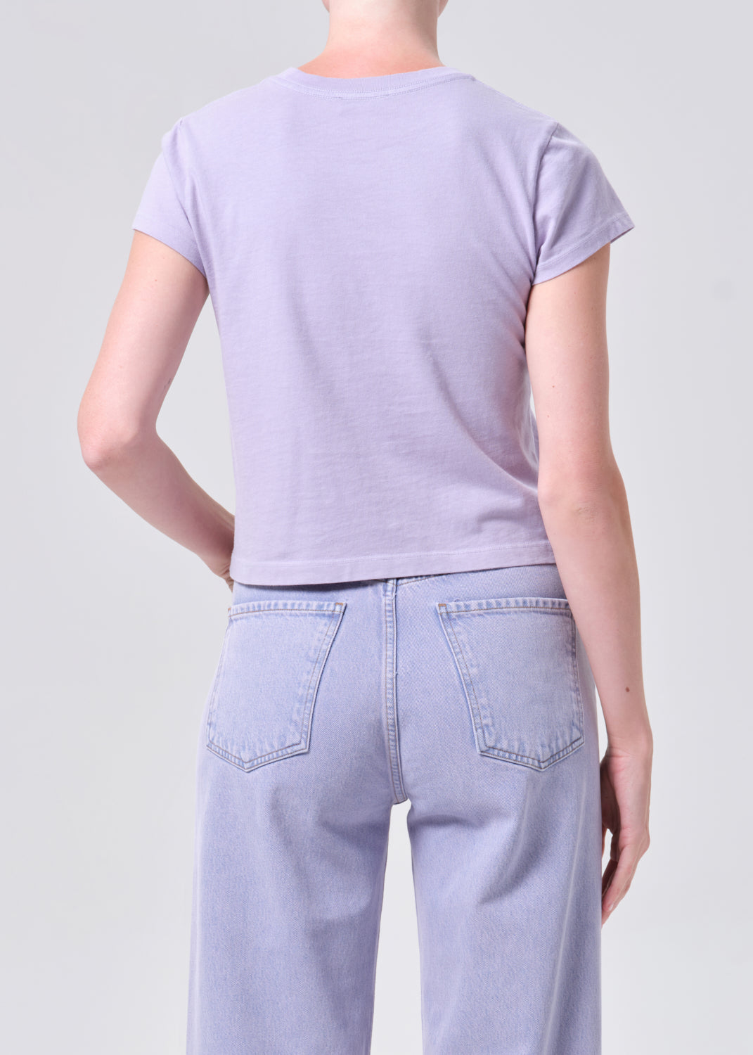 Person wearing a light purple t-shirt and jeans on a plain background