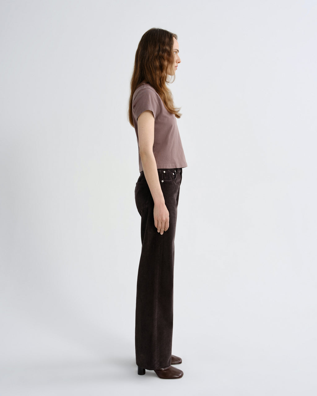 Woman wearing a brown top and dark pants on a white background