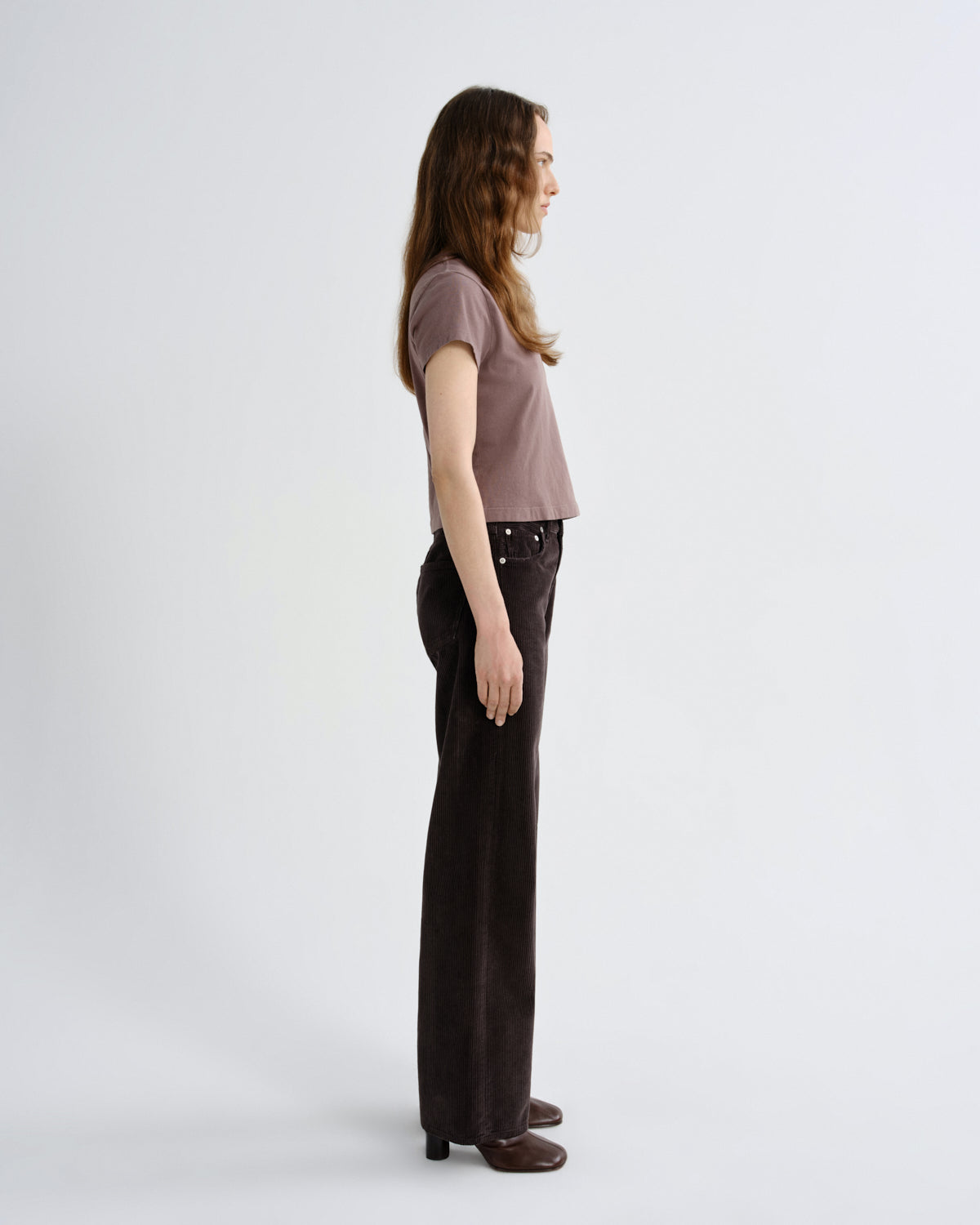 Woman wearing a brown top and dark pants on a white background