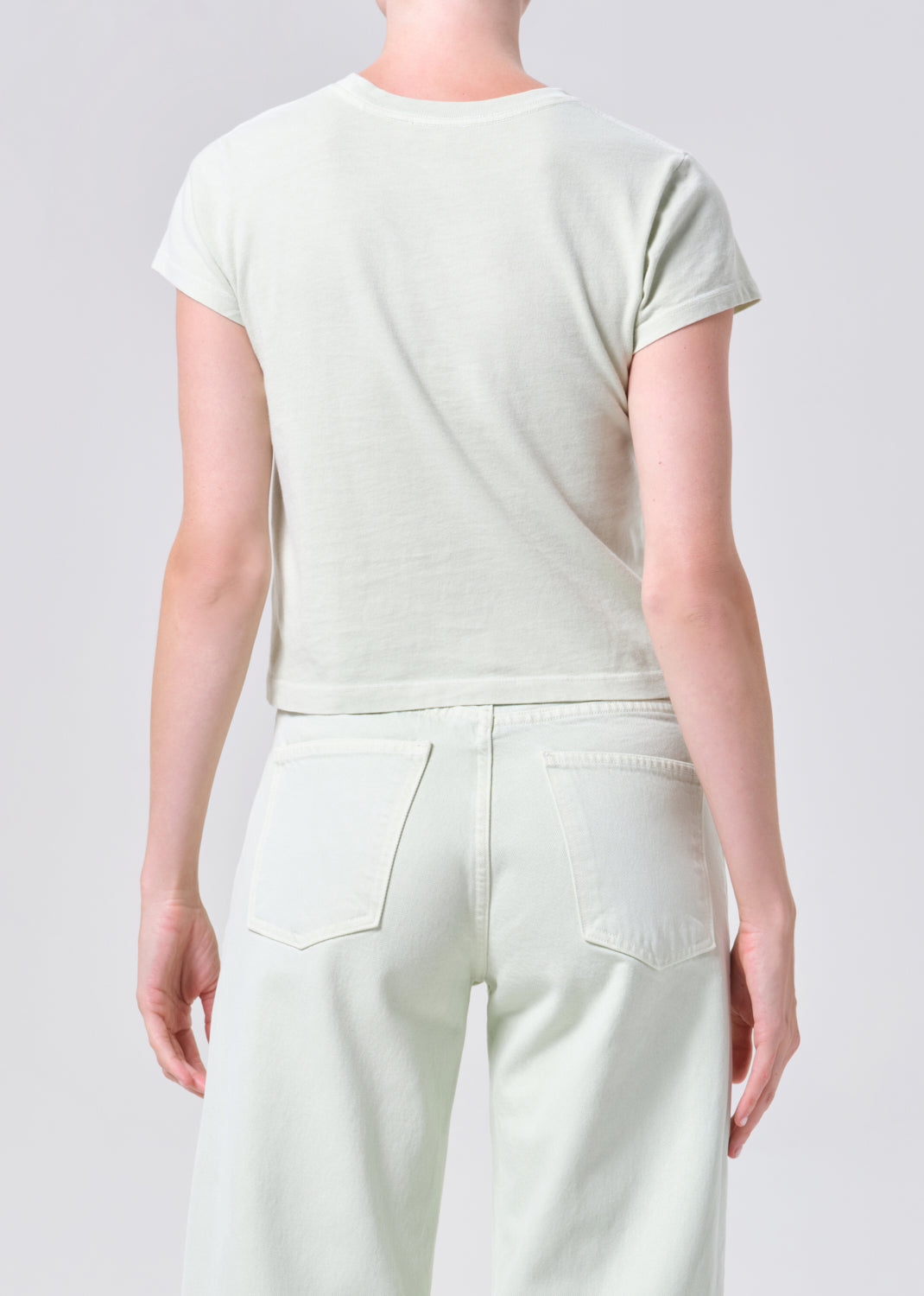 Person wearing a light green t-shirt and white pants on a plain background