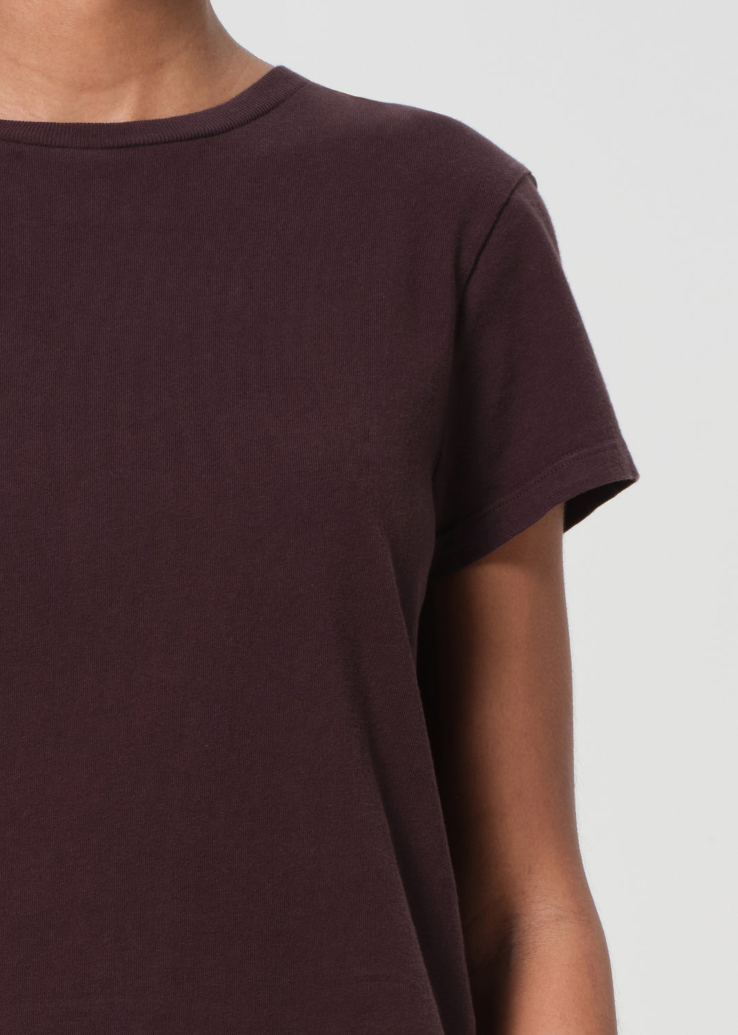 Close-up of a person wearing a plain dark brown t-shirt against a light gray background