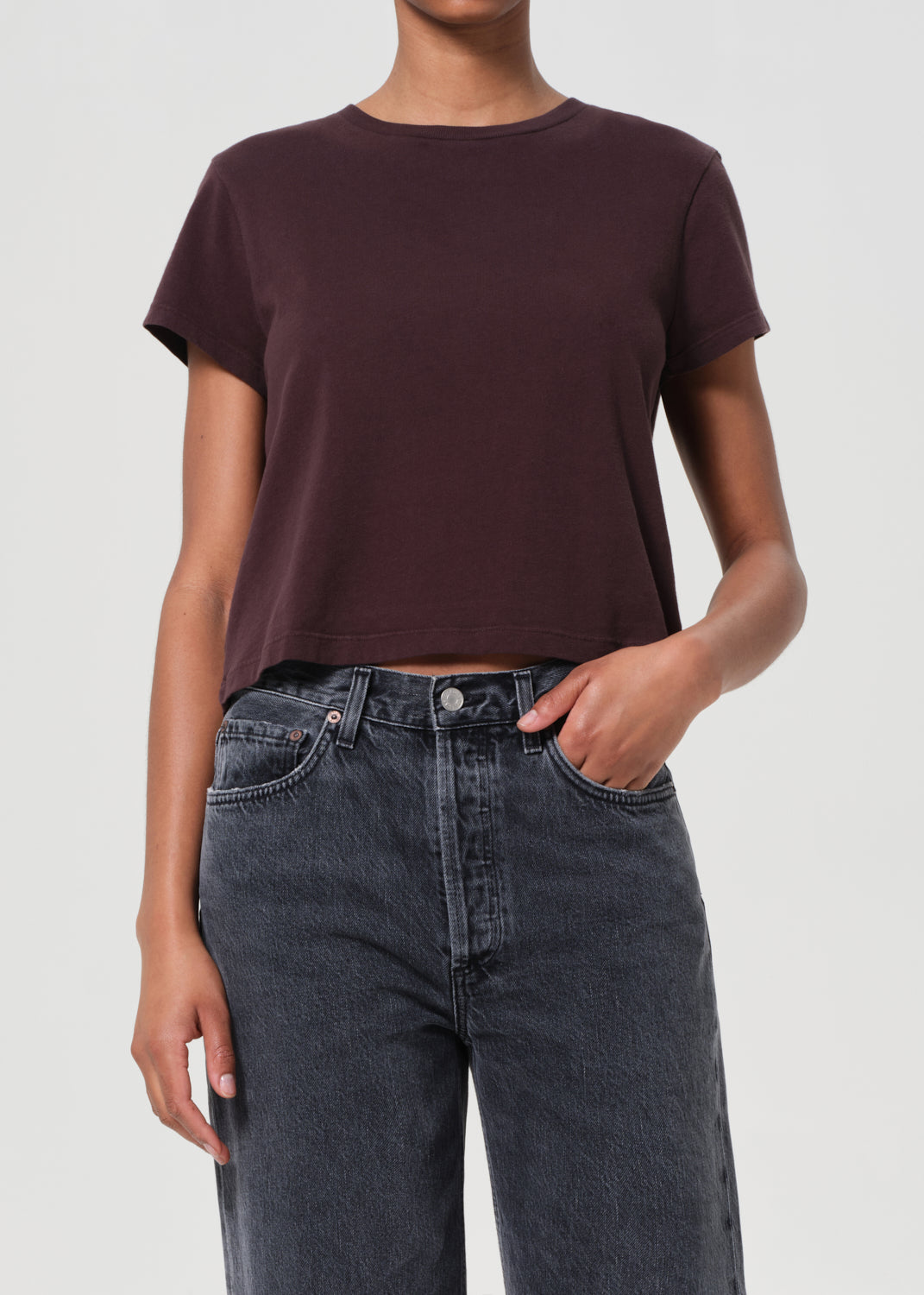 Person wearing a dark brown t-shirt and black jeans on a light gray background