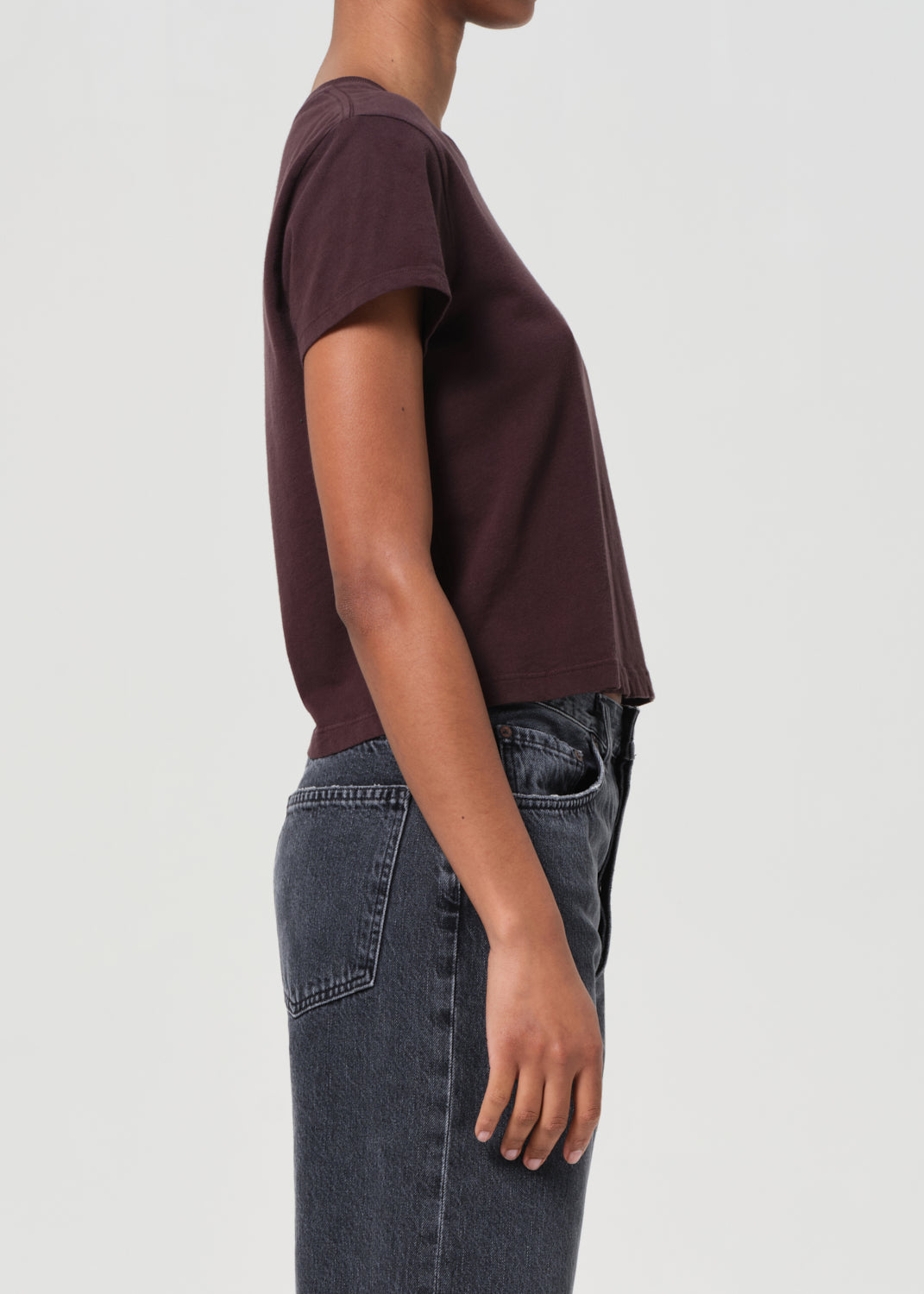 Person wearing a maroon t-shirt and dark jeans on a white background