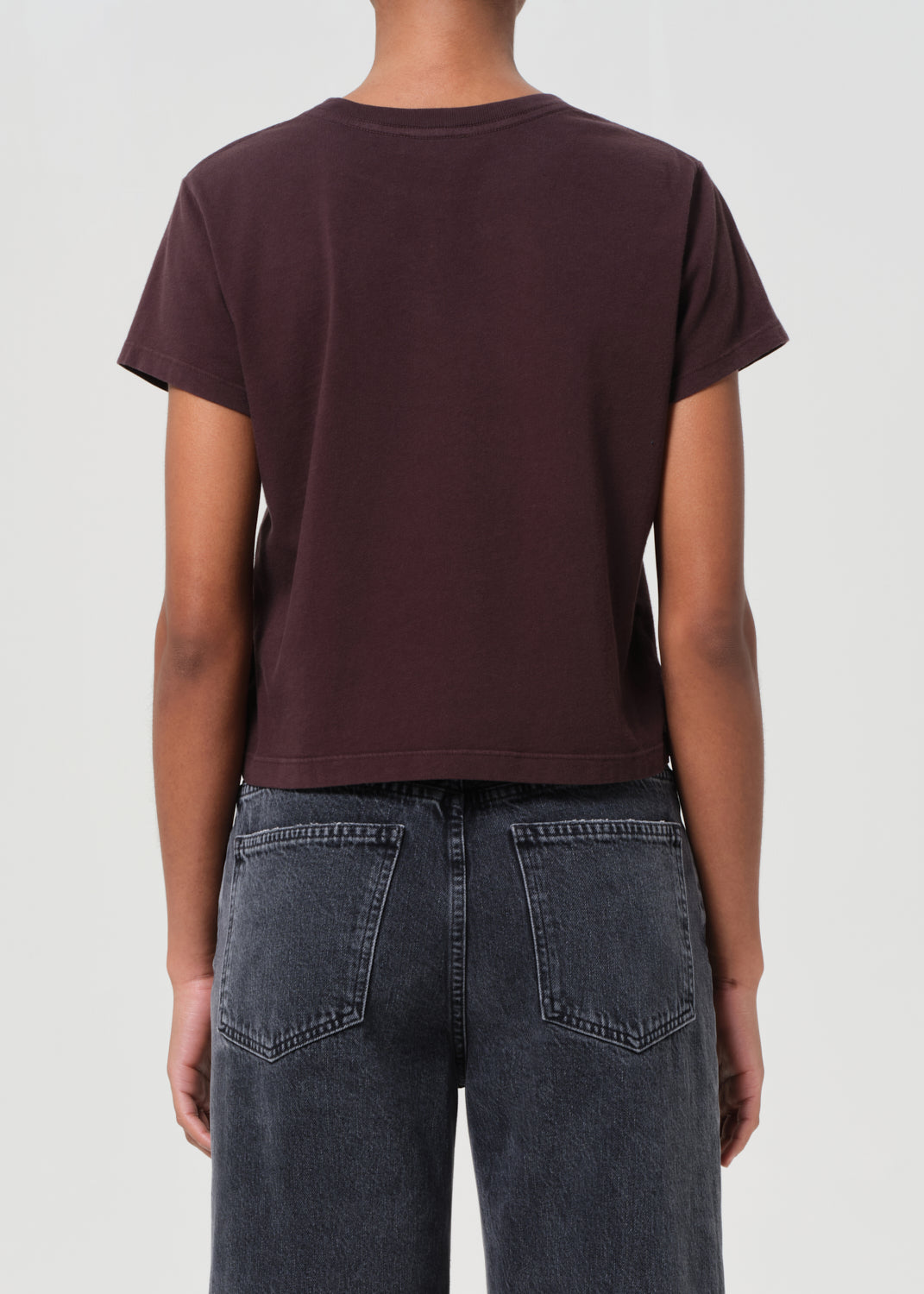 Person wearing a dark brown t-shirt and black jeans on a light gray background