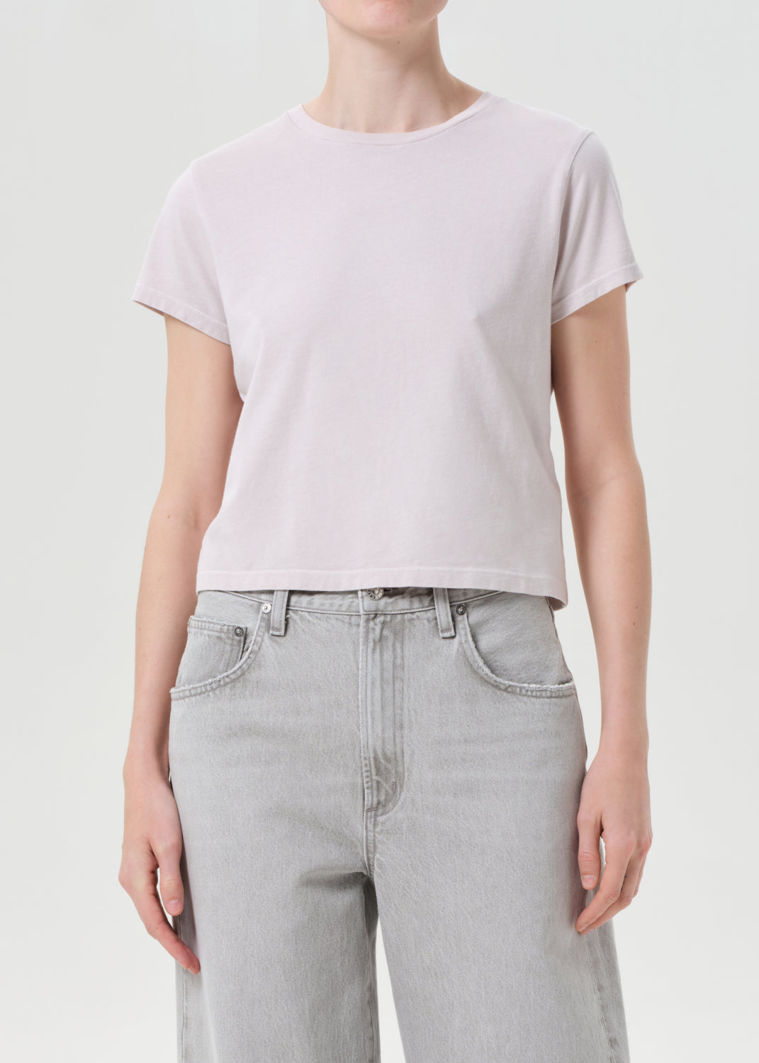 Person wearing a light purple t-shirt and light gray jeans on a plain background