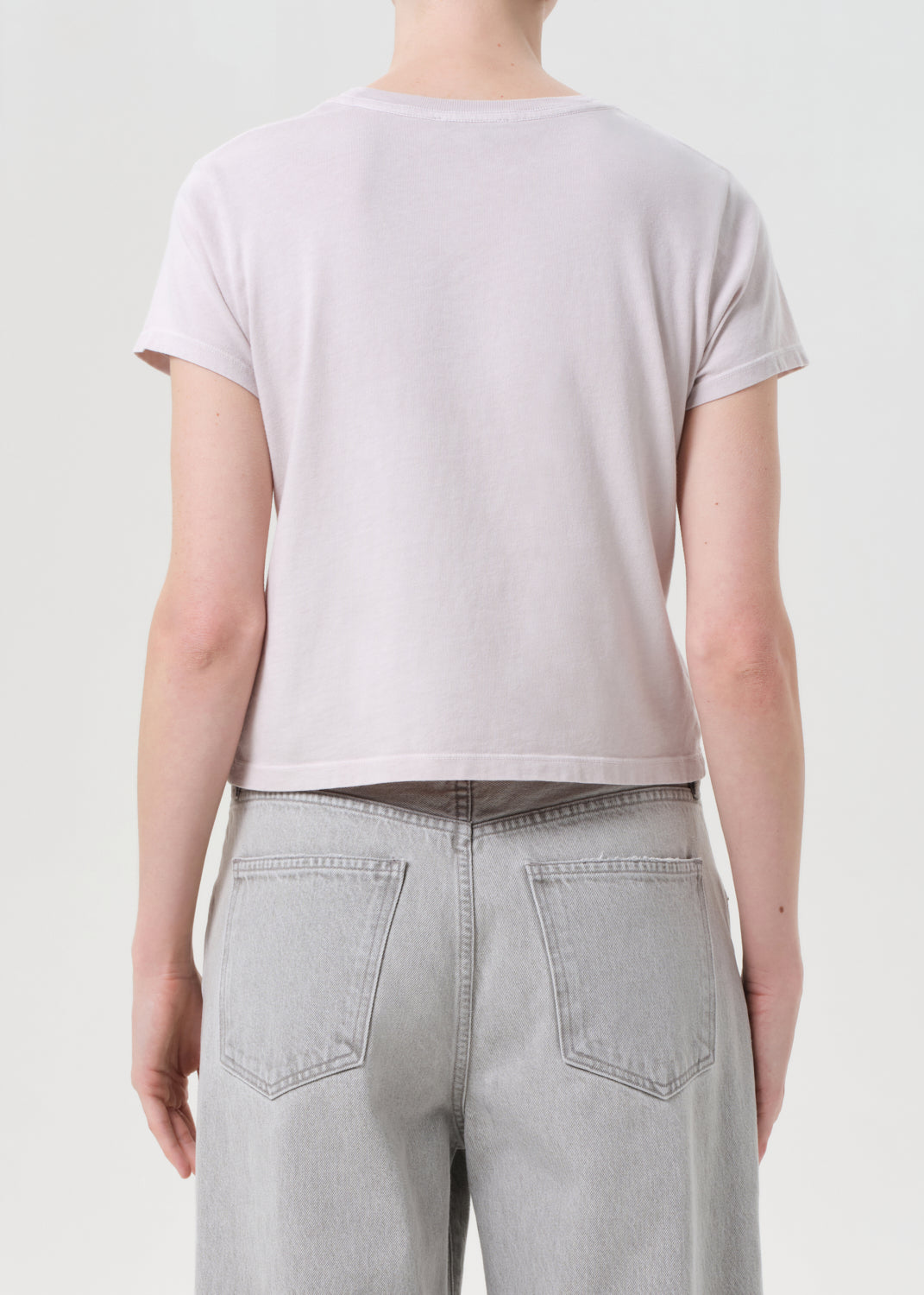 Person wearing a light purple t-shirt and light gray jeans on a plain background