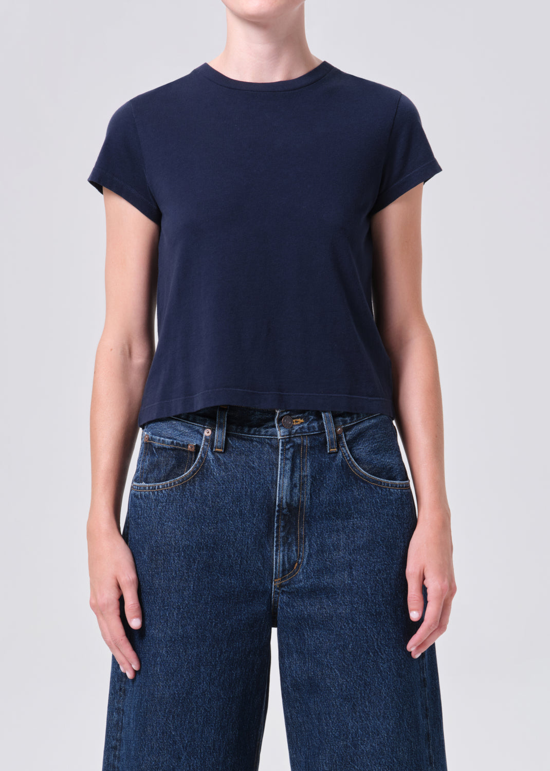 Person wearing a navy blue t-shirt and blue jeans on a light gray background