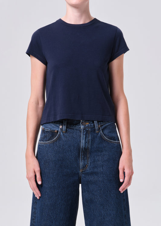 Person wearing a navy blue t-shirt and blue jeans on a light gray background