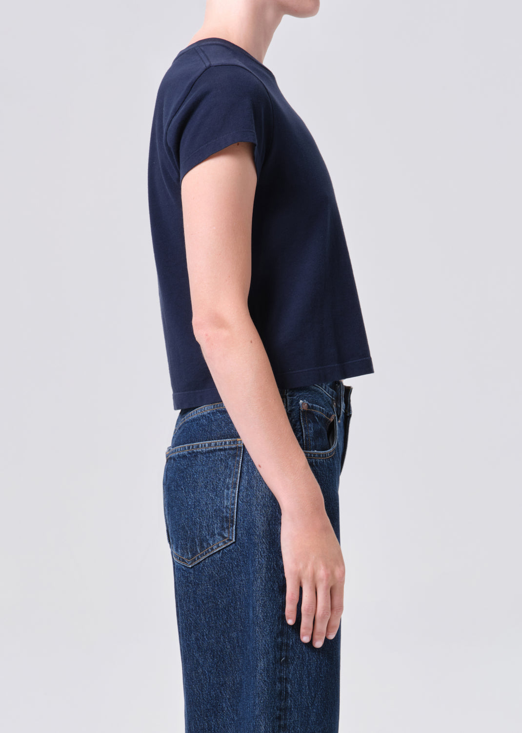 Person wearing a navy blue t-shirt and blue jeans on a light gray background