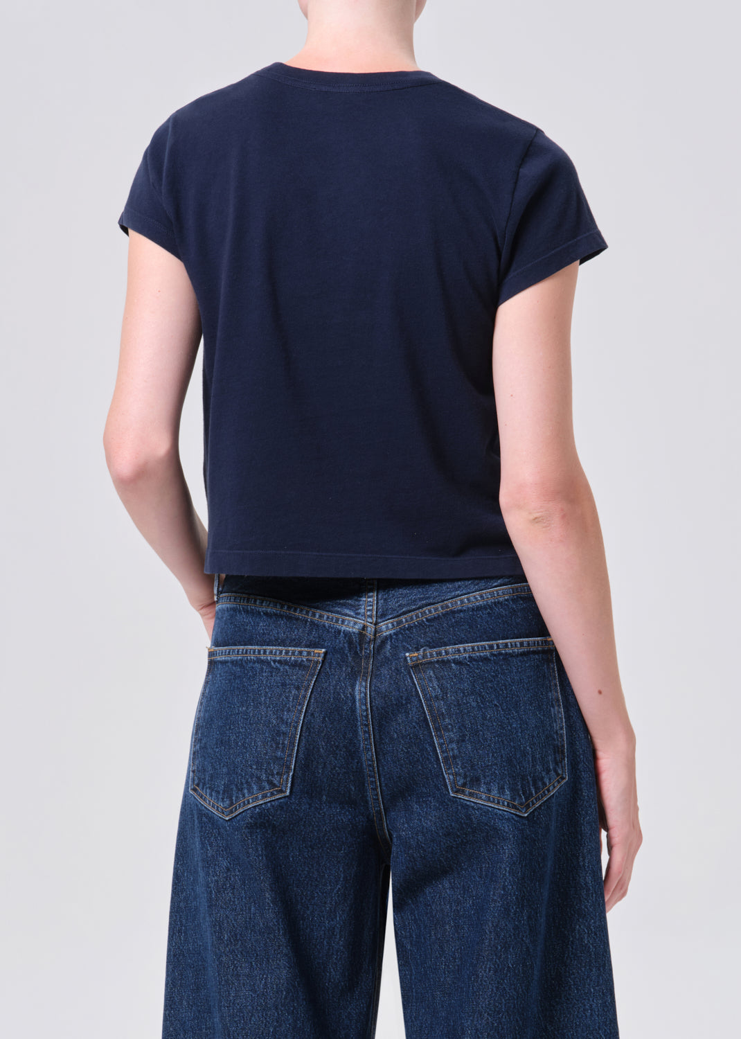 Person wearing a navy blue t-shirt and blue jeans on a light gray background