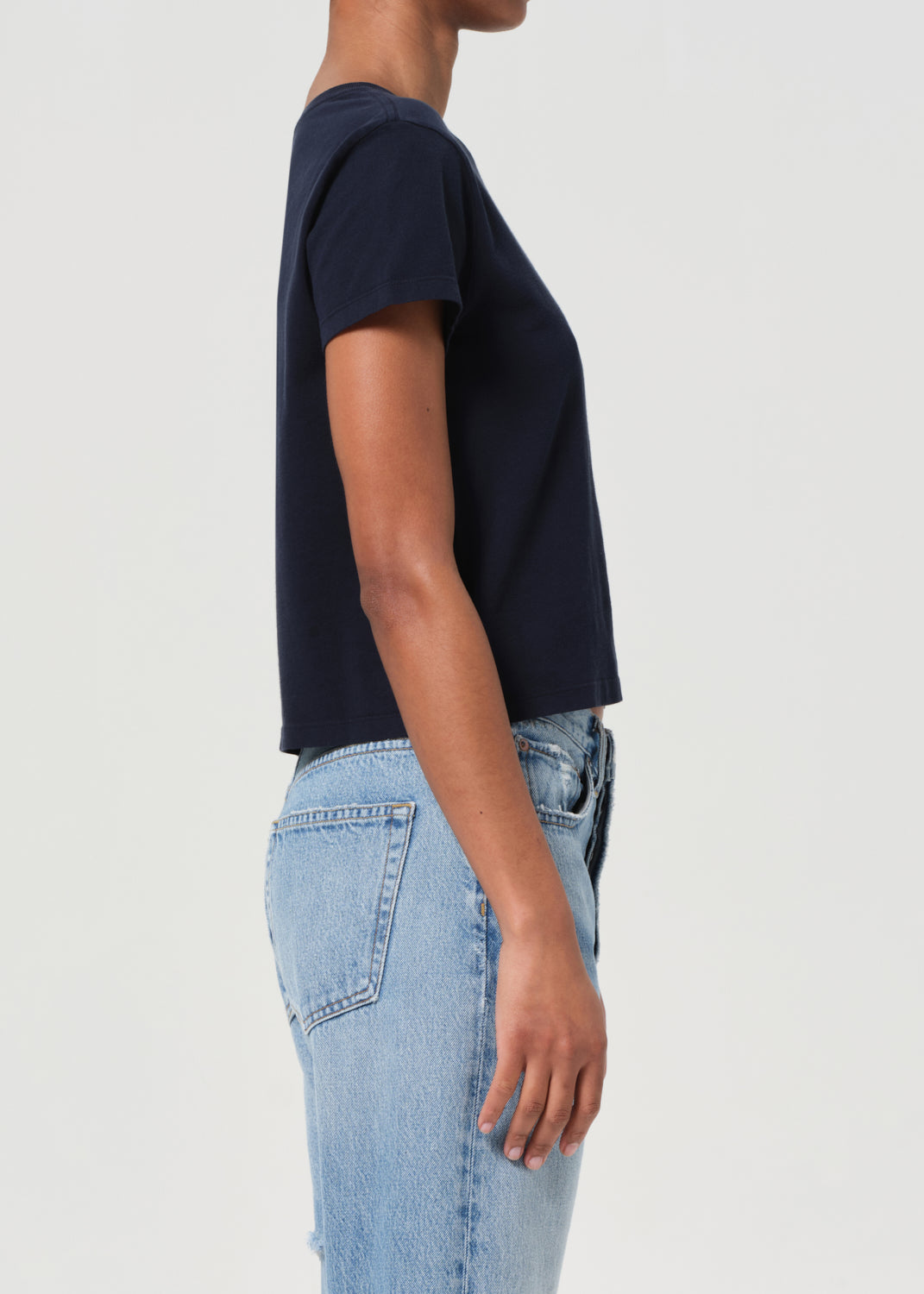 Person wearing a navy blue t-shirt and light blue jeans on a white background