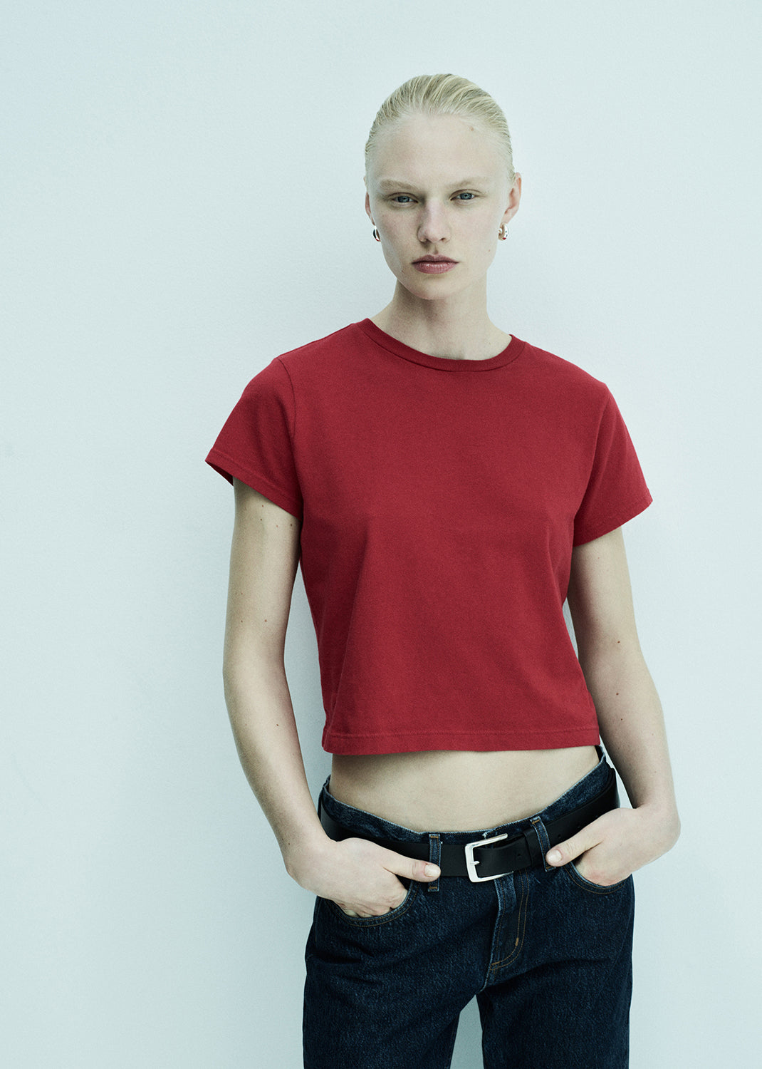 Person wearing a red t-shirt and dark jeans against a light background