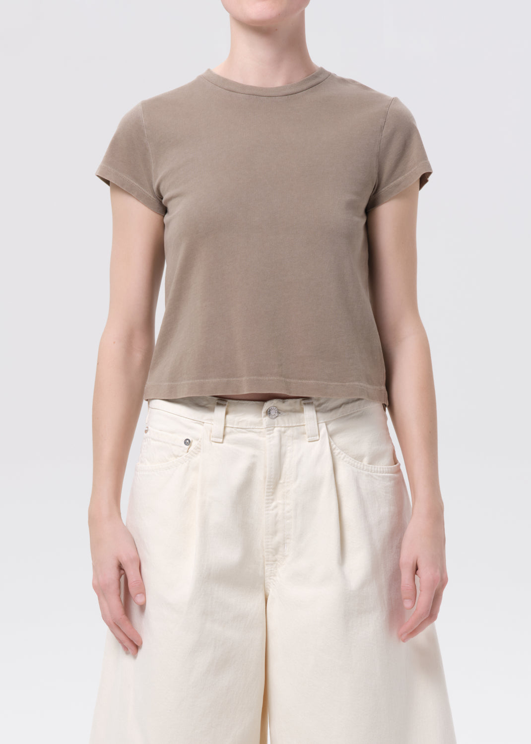 Person wearing a brown t-shirt and white pants on a plain background