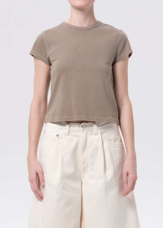 Person wearing a brown t-shirt and white pants on a plain background