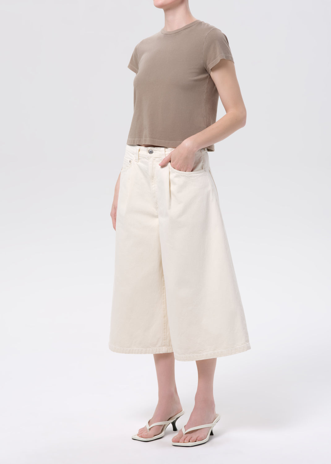 Person wearing a brown t-shirt and white wide-leg pants on a white background
