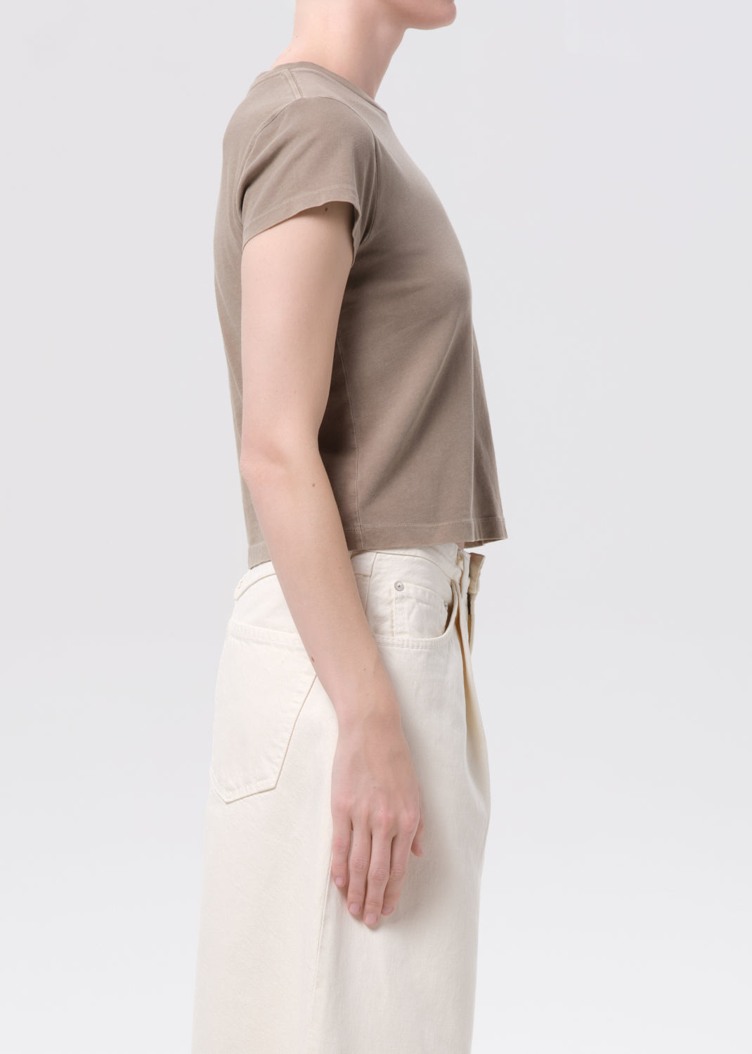 Person wearing a beige t-shirt and white pants on a light gray background