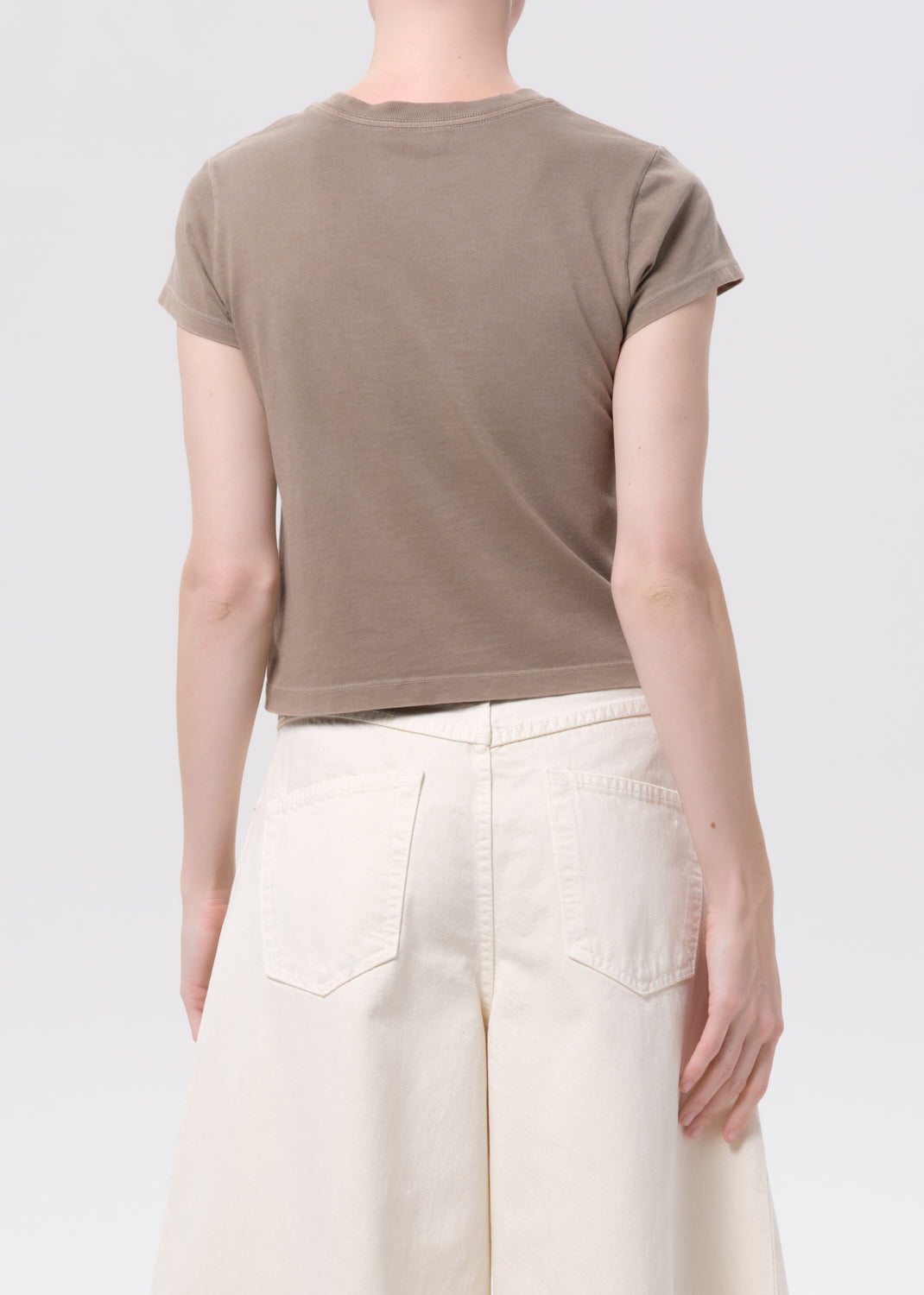 Person wearing a brown t-shirt and beige pants on a white background