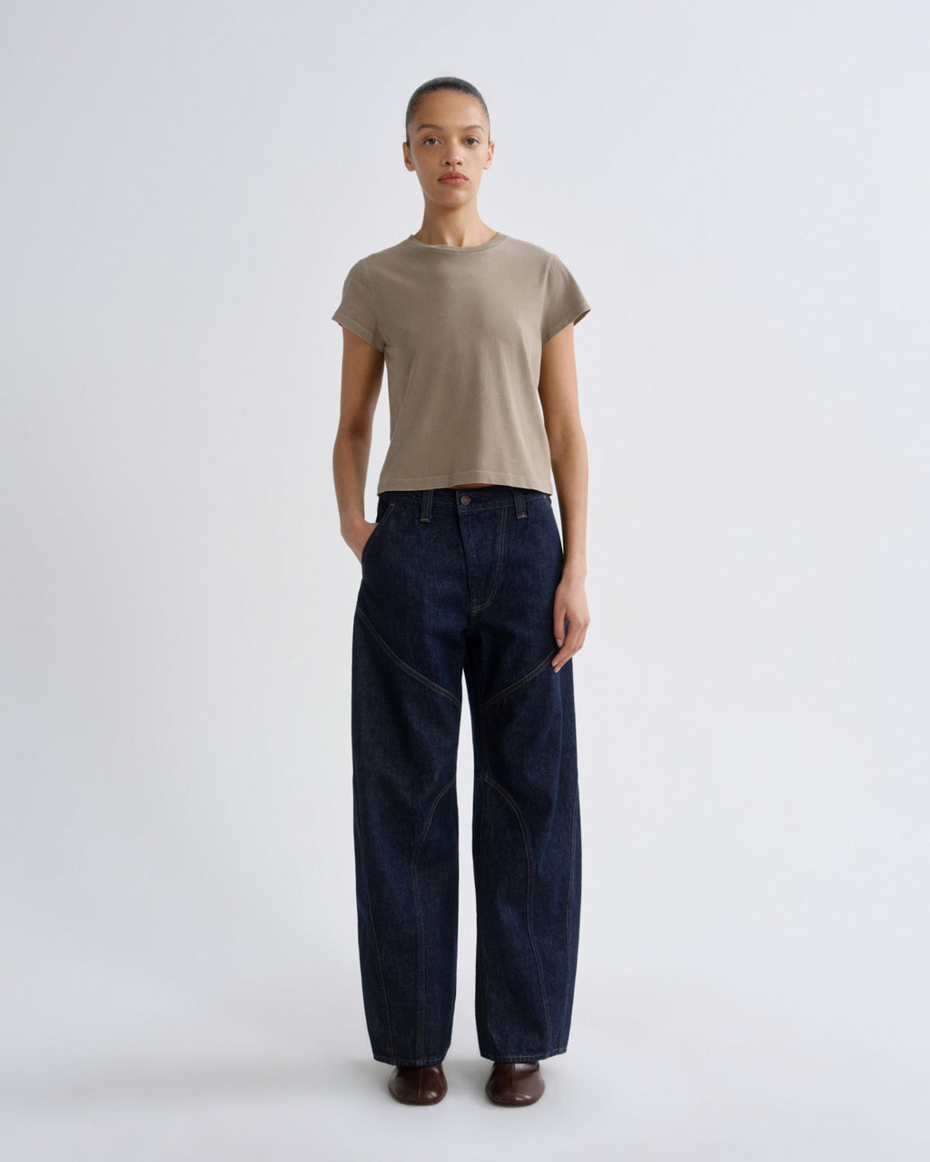 Person wearing a beige t-shirt and dark blue jeans on a white background