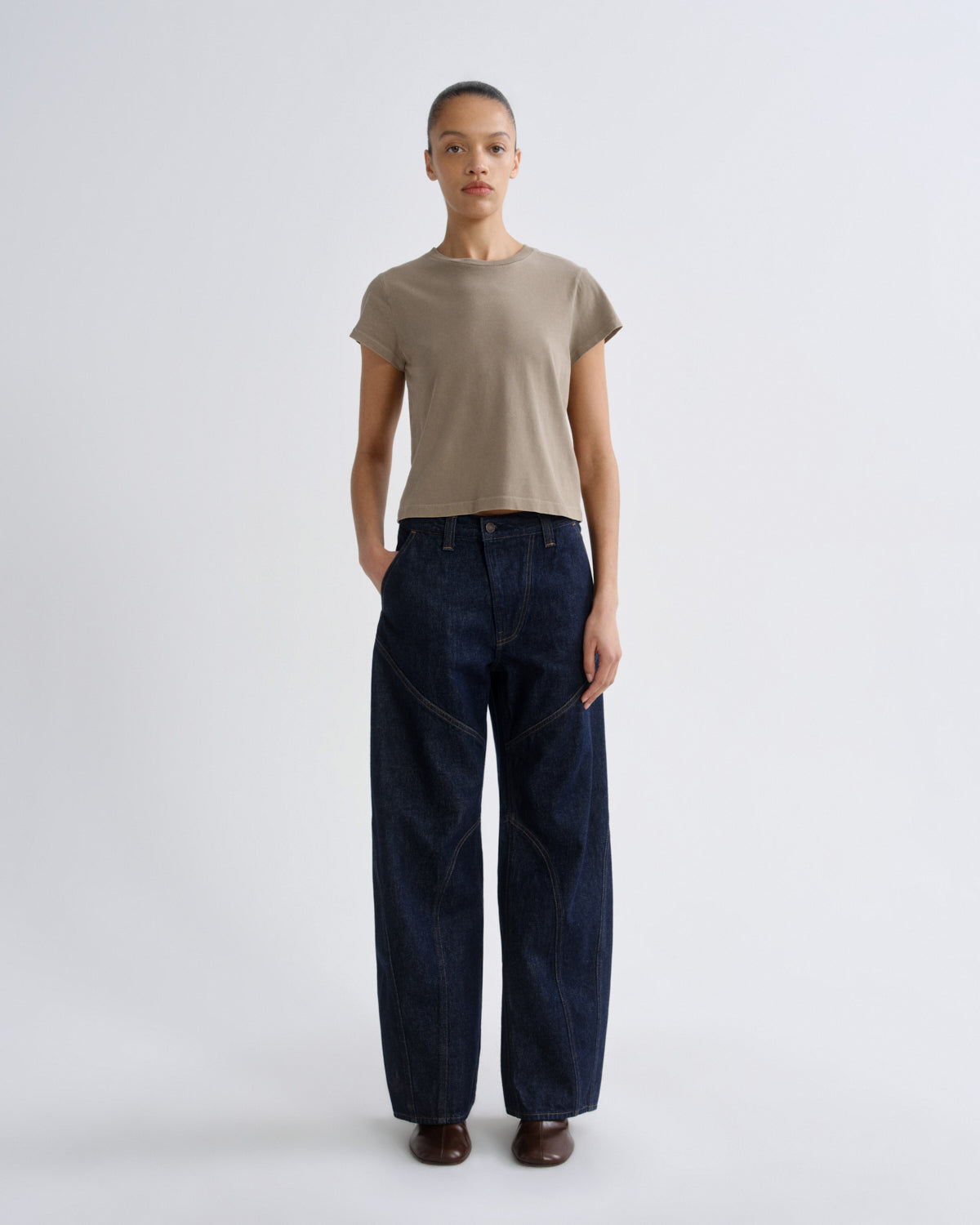 Person wearing a beige t-shirt and dark blue jeans on a white background