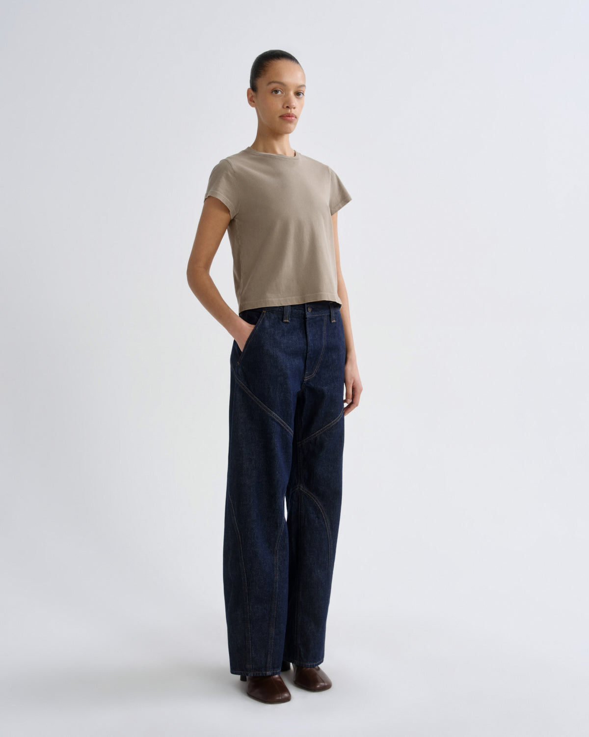 Person wearing a beige t-shirt and dark blue jeans on a white background