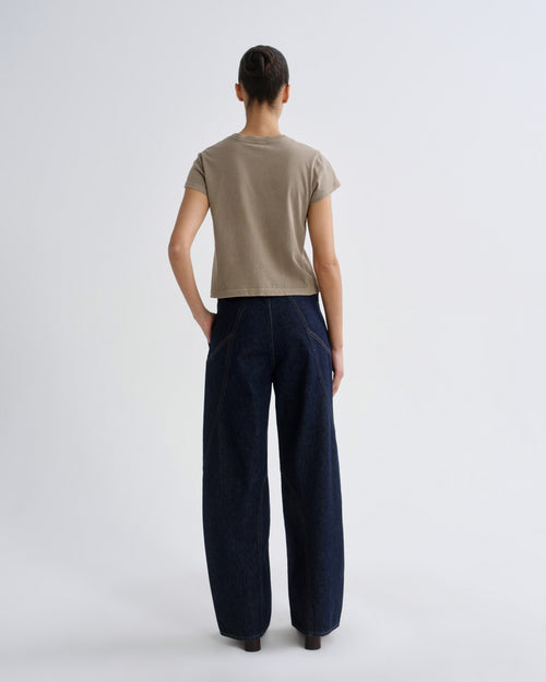 Person wearing a beige shirt and dark blue pants on a white background