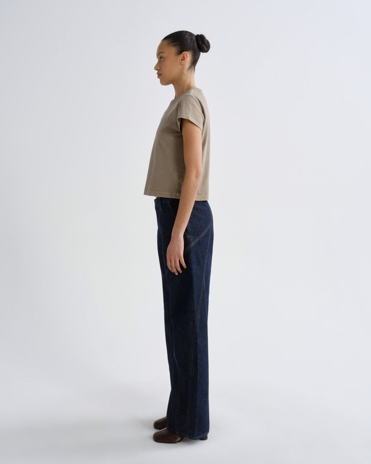 Person wearing a beige top and dark blue pants on a white background