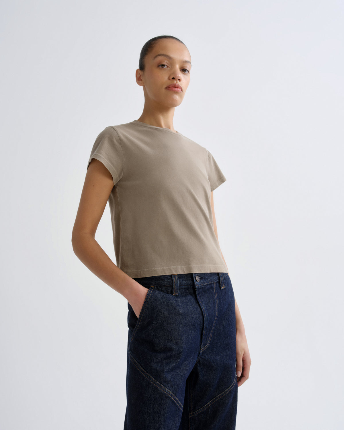 Person wearing a beige t-shirt and dark jeans on a white background