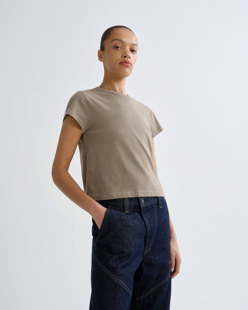 Person wearing a beige t-shirt and dark jeans on a white background