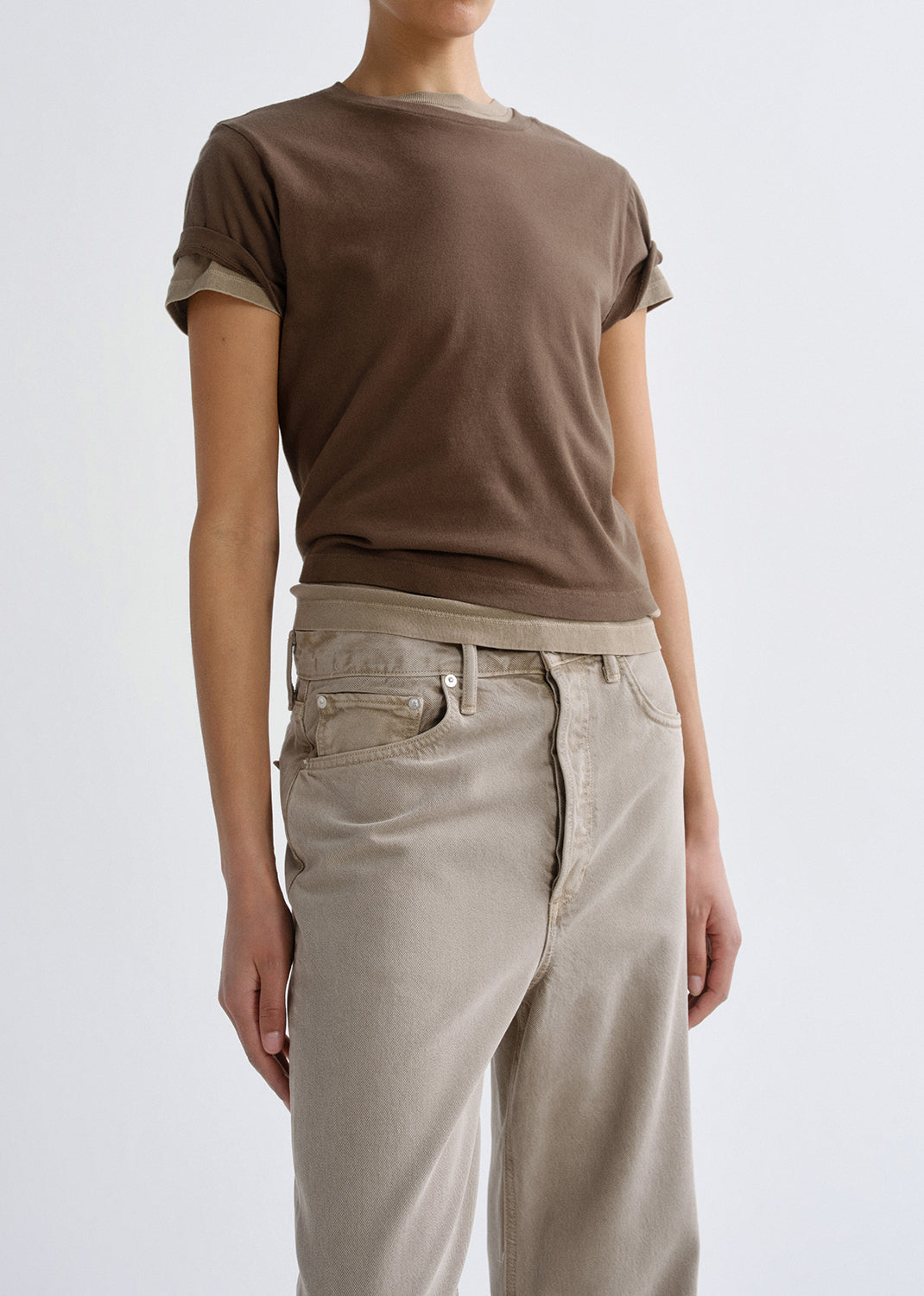 Person wearing a brown t-shirt and beige pants on a grey background