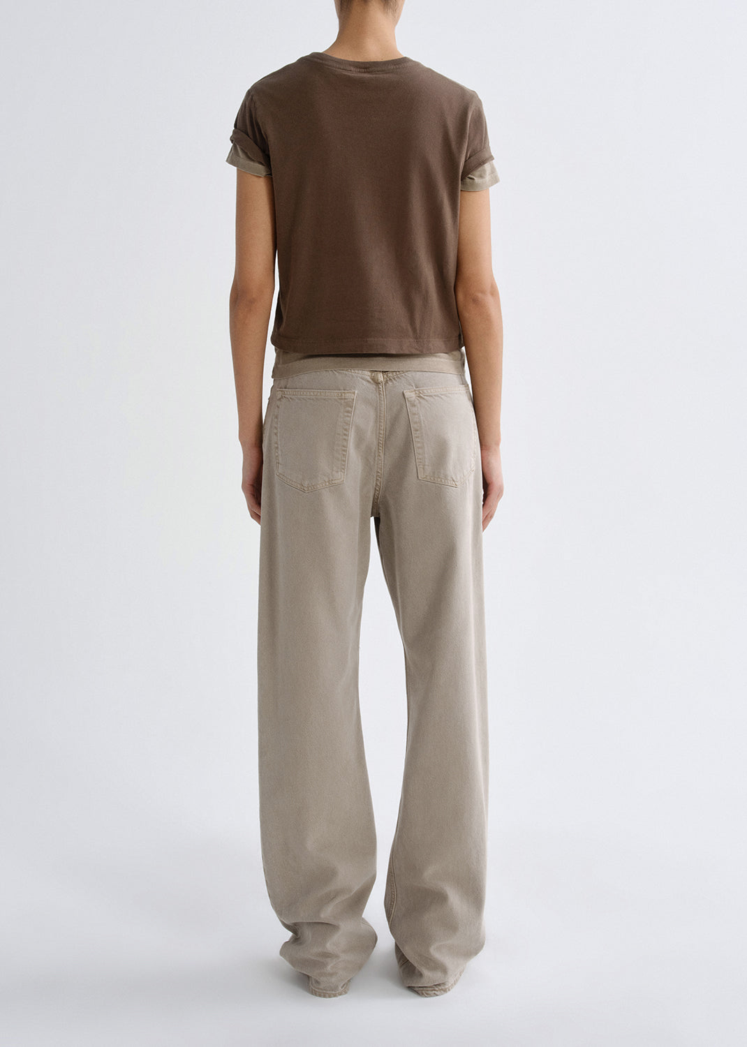 Person wearing a brown t-shirt and beige pants on a grey background