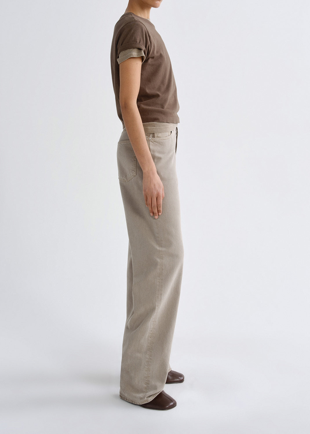 Person wearing a brown t-shirt and beige pants on a grey background