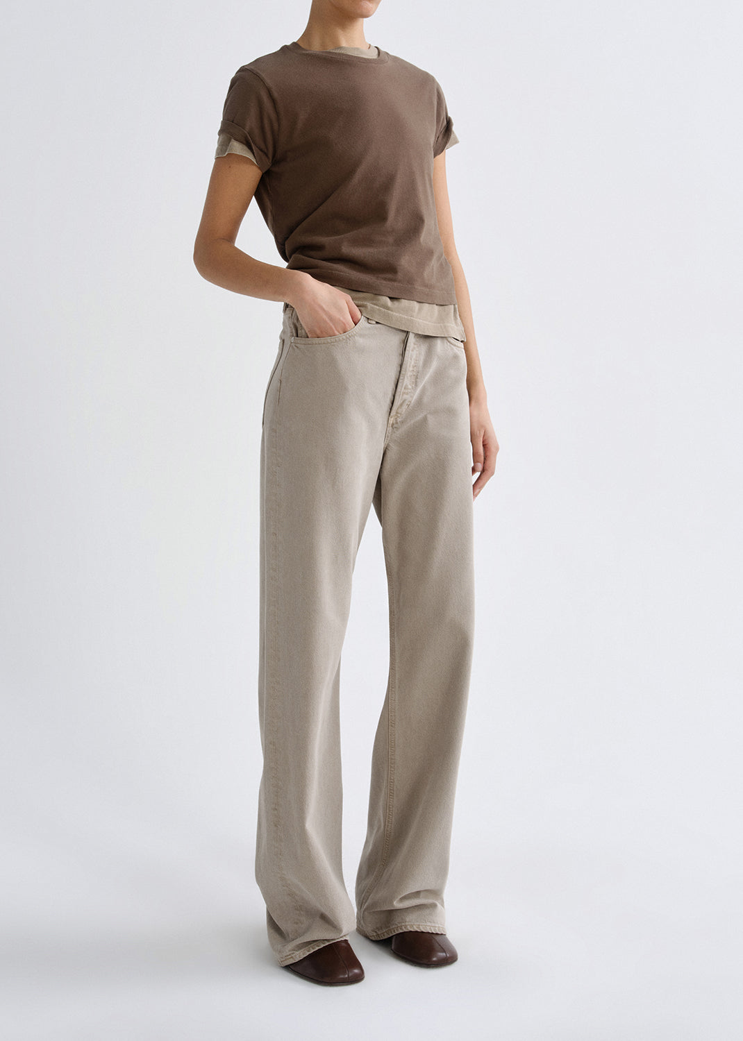 Person wearing a brown t-shirt and beige pants on a grey background