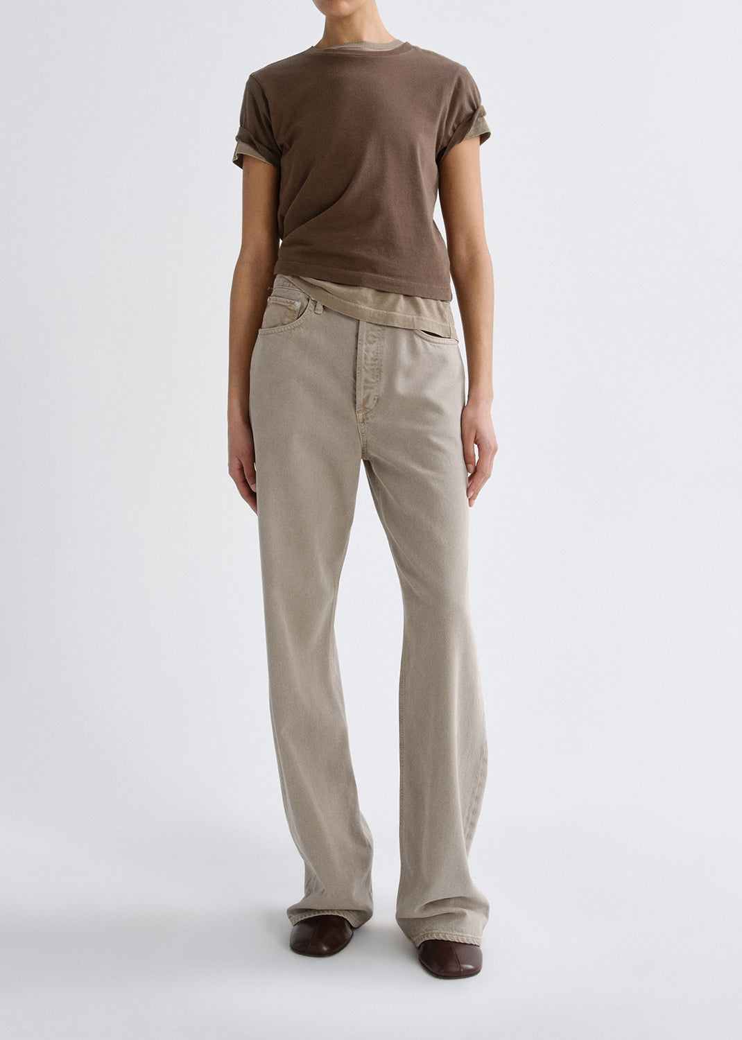 Person wearing a brown t-shirt and beige pants on a grey background