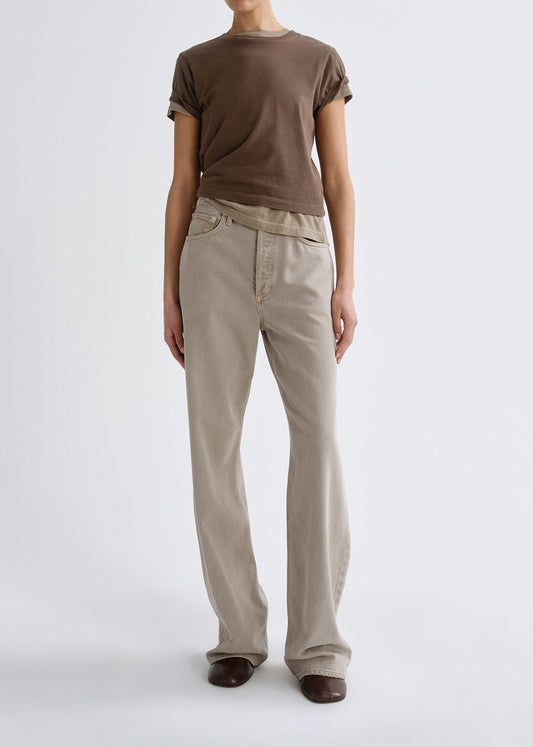 Person wearing a brown t-shirt and beige pants on a grey background