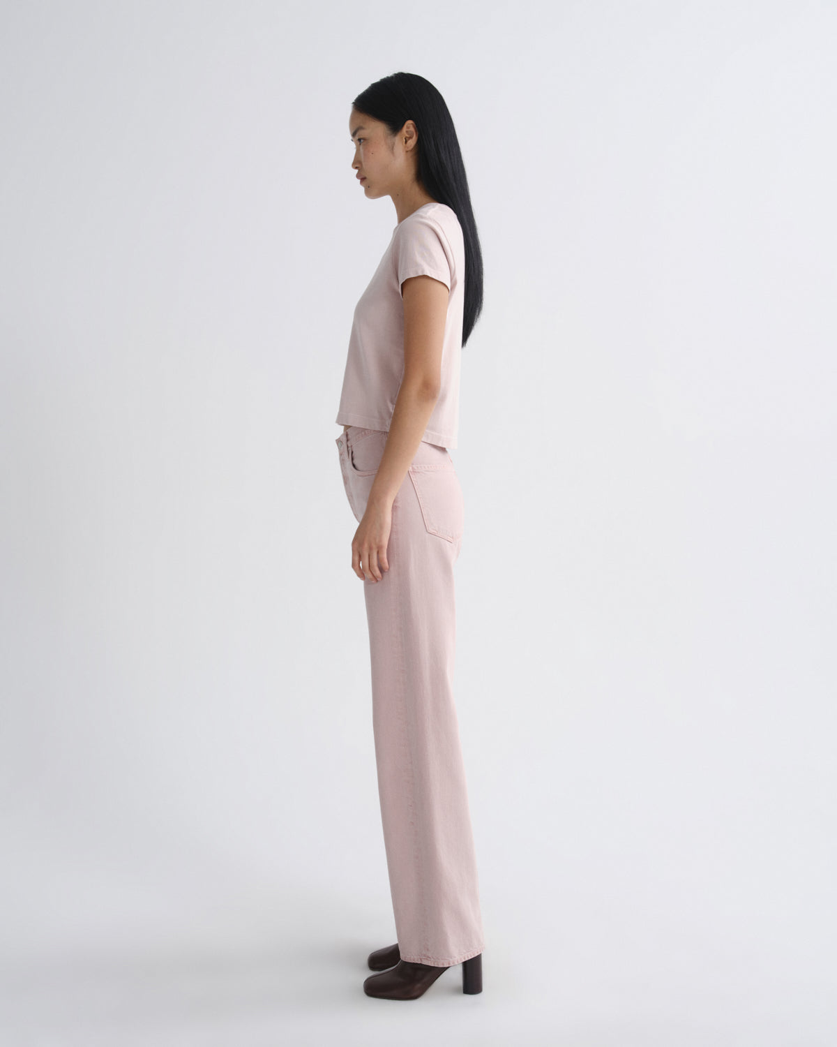 Woman wearing a beige top and light pink pants on a white background