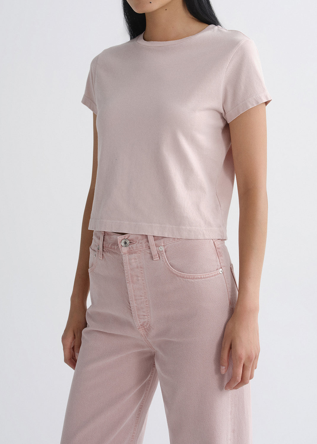 Person wearing a light pink short sleeve crewneck tee with light pink straight leg jeans on a white background